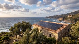 Maison corse en pierre avec panneaux solaires photovoltaïques sur toit en tuiles canal, exposée au vent libeccio sur la côte méditerranéenne en Corse